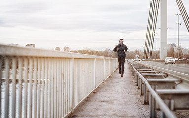 A young man running on a bridge. Guy keeping his body fit by jogging in an urban city environment...