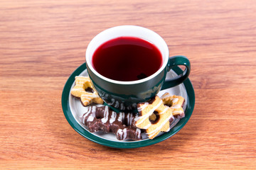 A cup of fragrant black tea in a porcelain mug and shortbread covered with chocolate on a plate - delicious breakfast for your favorite.
