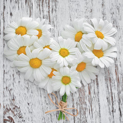 Obraz premium White daisies in the shape of a heart on the old wooden background. 