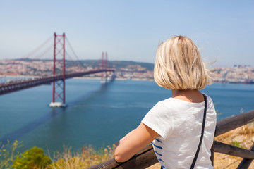 Fototapeta na wymiar Female traveler standing next to the statue of National Sanctuary of Christ the King and enjoys panoramic views of Lisbon and the bridge of April 25.