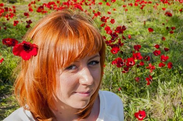 Naklejka premium Pretty girl with a red flower behind her ear at the anemone flowering field. Flowering Negev Desert in Israel.