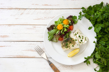 Fried cod fillet and salad in plate on white wooden background
