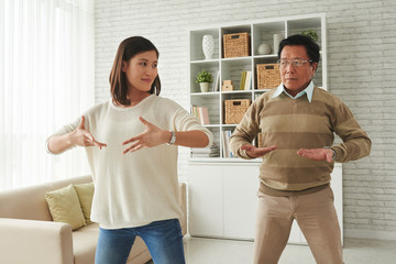Obraz premium Portrait of pretty young woman and her senior father standing in living room and doing breathing exercises