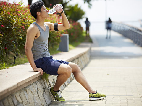young asian jogger resting and drinking water