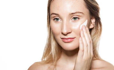 Young woman applies moisturizer to protect delicate skin on a white background