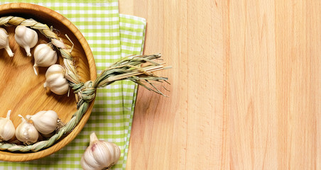 Braid of garlic in wooden plate on a fabric green plaid cloth on a light wooden table.