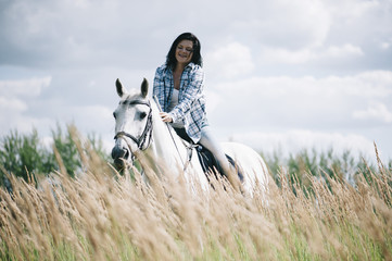 Happy brunette woman riding her white stallion, having fun at the summer field