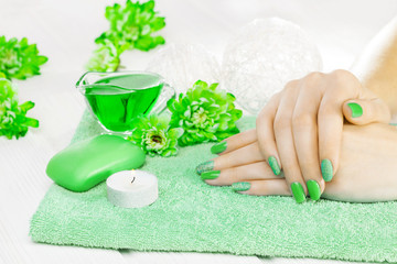 Obraz na płótnie Canvas beautiful green manicure with chrysanthemum and towel on the white wooden table. spa