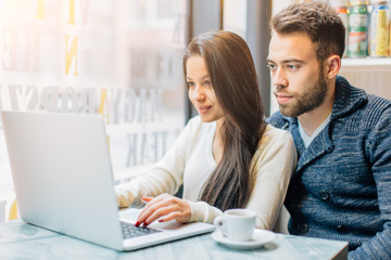 Young couple sitting at cafe and looking at laptop
