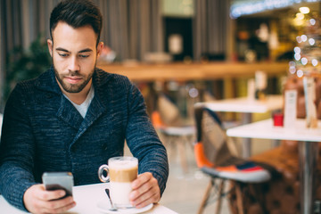 Young man sitting at cafe and using mobile phone 