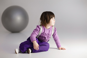 Naklejka premium little girl in purple clothes with big ball for fitness on gray 