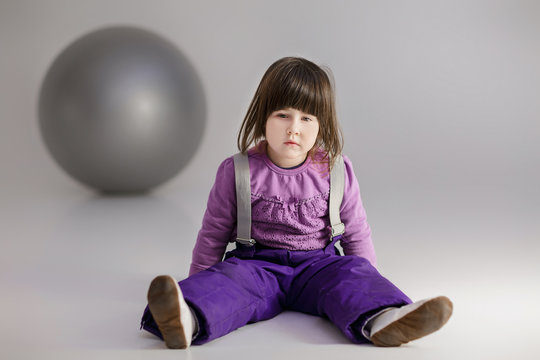little girl in purple clothes with big ball for fitness on gray 