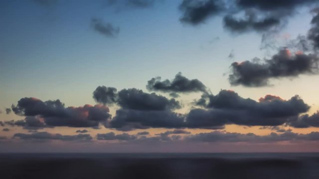 time lapse of clouds crossing the amazing sky over the sea or ocean at sunset. transition from day to night. The clouds cross slowly from left to right colored yellow orange purple blue