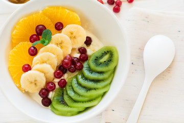 Healthy breakfast: fresh cottage cheese with orange,banana, kiwi, cranberry and honey on white wooden table. Selective focus