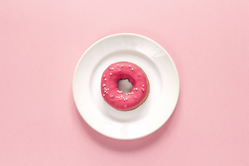 Donut with icing on plate on pink background. Top view.