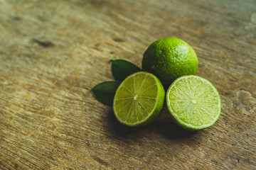 Fresh limes in a bowl with leaves cut in half on wooden table, Top view, background.