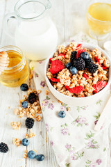 
healthy and hearty breakfast of muesli , oatmeal or granola with berries , blackberries , blueberries and strawberries , honey , milk and green tea on a wooden background