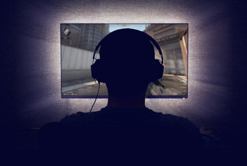 Gamer in headphones sits in front of a blank monitor in dark room - obrazy, fototapety, plakaty