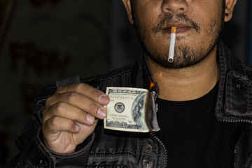 Handsome man lighting his cigar with dollar note. Concept idea.