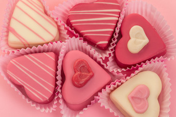 Pink heart shaped petit fours cakes seen from above on a pink background