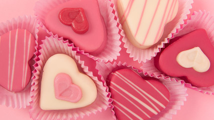 Pink heart shaped petit fours cakes seen from above in a banner size frame on a pink background