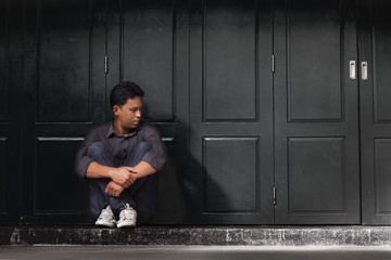 Asian young man with depression sitting beside wall. process in dark tone