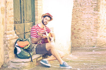 Traveler man playing guitar sitting in old italian town next at  retro house - Young musician on summer journey street photography - Nostalgic concept with vintage filter effect and soft  tones