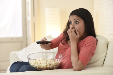 Naklejka premium latin woman sitting at home sofa couch in living room watching television scary horror movie