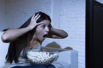 Naklejka premium latin woman at home sofa couch in living room watching television scary horror movie or suspense thriller