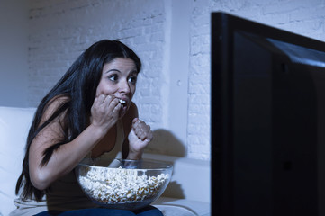 Naklejka premium latin woman at home sofa couch in living room watching television scary horror movie or suspense thriller