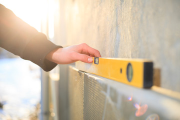 Young builder man hand measuring wall of house by professional yellow building measure