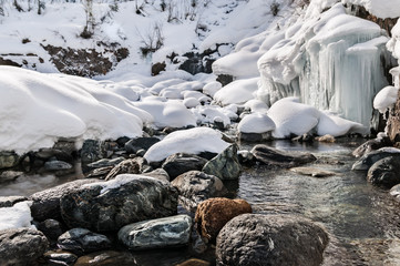 Winter landscape of mountain river with stones and small frozen waterfall