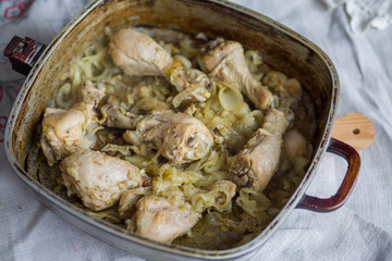 Chicken legs braised with spices and onion in a pan in the oven.