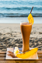 Homemade banana chocholate drink, frontal view. Sand beach and sea in background. Selective focus.