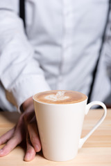 Waiter with suspenders handing over Cappuccino, closeup of cup, selective focus
