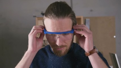 Young man working as carpenter and put eye protection glasses on, slow motion
