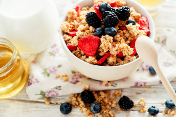 
healthy and hearty breakfast of muesli , oatmeal or granola with berries , blackberries , blueberries and strawberries , honey , milk and green tea on a wooden background