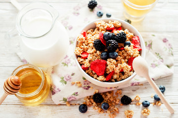 
healthy and hearty breakfast of muesli , oatmeal or granola with berries , blackberries , blueberries and strawberries , honey , milk and green tea on a wooden background