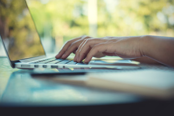 Fototapeta premium Closeup image of a hands working and typing on laptop keyboard with blur nature background