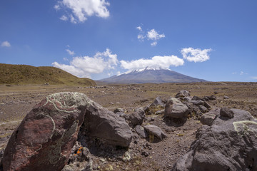 The snowcapped Cotopaxi Volcano in the Ecuadorian Andes with lichen encrusted boulders in the foreground. Vapour is rising from the crater.