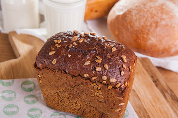 Close up rye bread with sunflower seeds and assortment of breads and glass of milk on the background . Selective focus