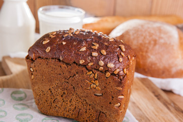 Close up rye bread with sunflower seeds and assortment of breads and glass of milk on the background . Selective focus
