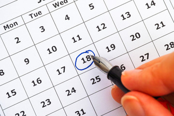 Fountain pen in woman hand marking day on calendar