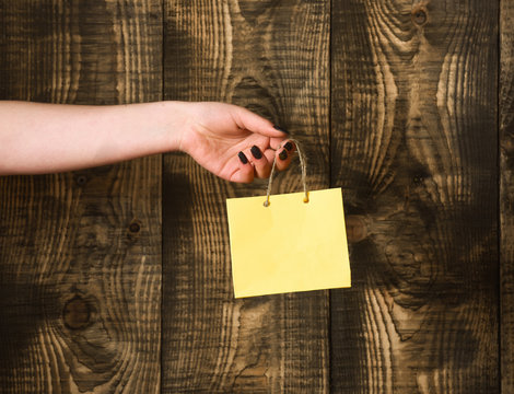 yellow shopping bag in female hand on wooden background