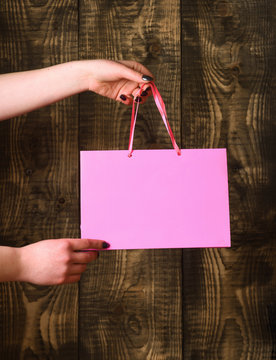 pink shopping bag in female hands on wooden background