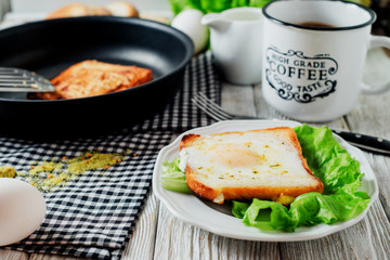 a delicious and hearty breakfast, fried eggs in a white toast with spices, peppers, lettuce, a cup of black coffee and milk on a wooden background 