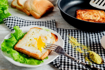 a delicious and hearty breakfast, fried eggs in a white toast with spices, peppers, lettuce, a cup of black coffee and milk on a wooden background 