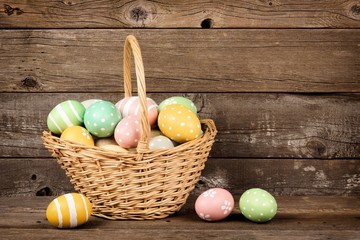 Obraz na płótnie Canvas Easter basket filled with hand painted eggs over a rustic wooden background