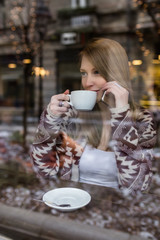 Beautiful woman sitting alone in cafeteria, drinking coffee and talking on cell phone. 