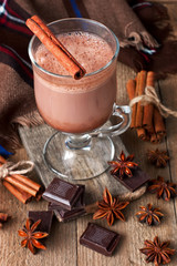 Obraz na płótnie Canvas Glass mug of hot chocolate, cinnamon sticks, nuts and chocolate on wooden table 